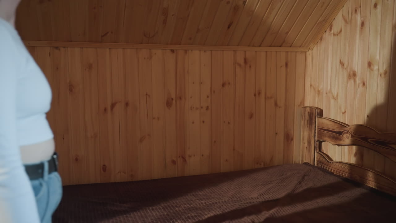 young girl wearing white top and denim touching bed surface while sitting in cozy wood paneled room, exploring texture with hands, calm indoor moment in rustic setting filled with natural light