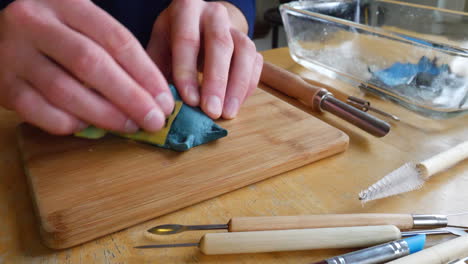 an artist in a messy studio using wet sandpaper while sanding and polishing a polymer clay sculpture project of a handmade mask figurine with tools and brushes on the desk