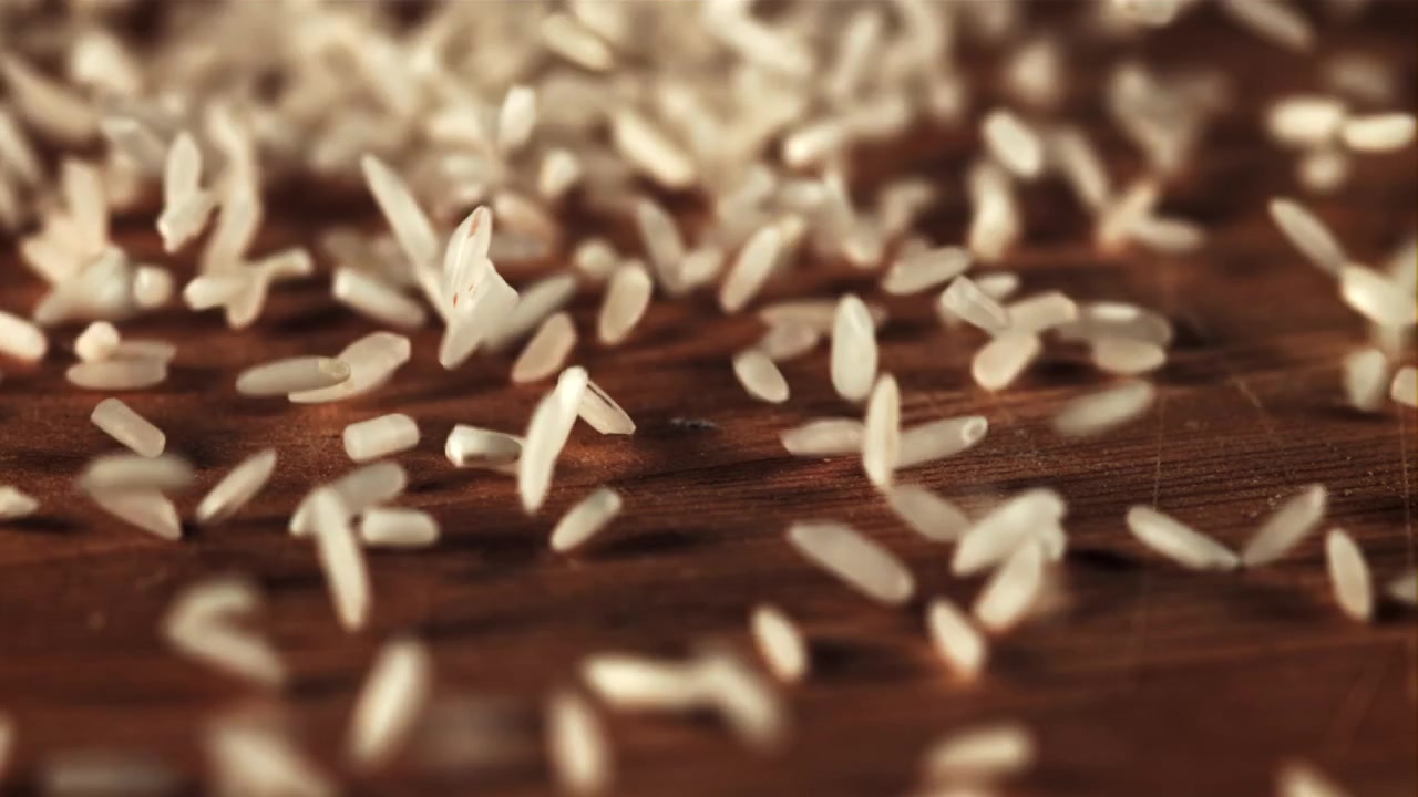 Chicchi di riso bianco crudo che cadono su una superficie di legno scuro.