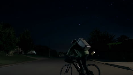 a lone cyclist delivers at night in a suburban neighborhood
