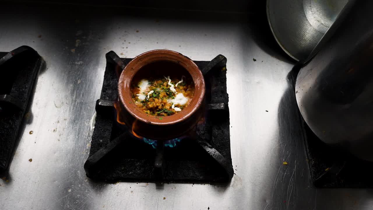 Chicken handi with cream and herbs simmers in clay pot over flame at Pakistani restaurant. Lahore, Pakistan