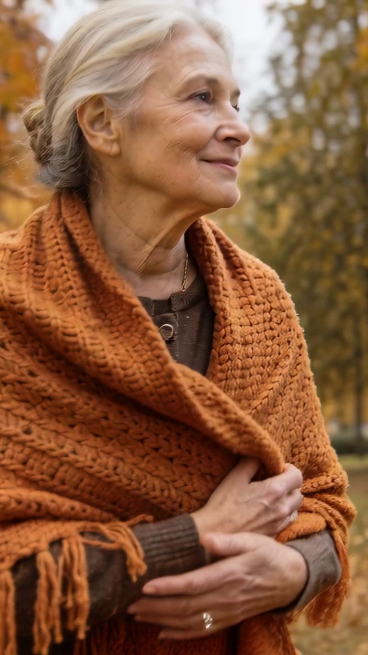 Vertical video: Spotting movement right, senior woman adjusting orange shawl in park, staying warm