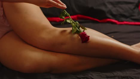 Eine-Sinnliche-Frau-In-Sexy-Dessous-Streichelt-Verführerisch-Ihr-Bein-Mit-Einer-Roten-Rose,-Während-Sie-Im-Bett-Posiert