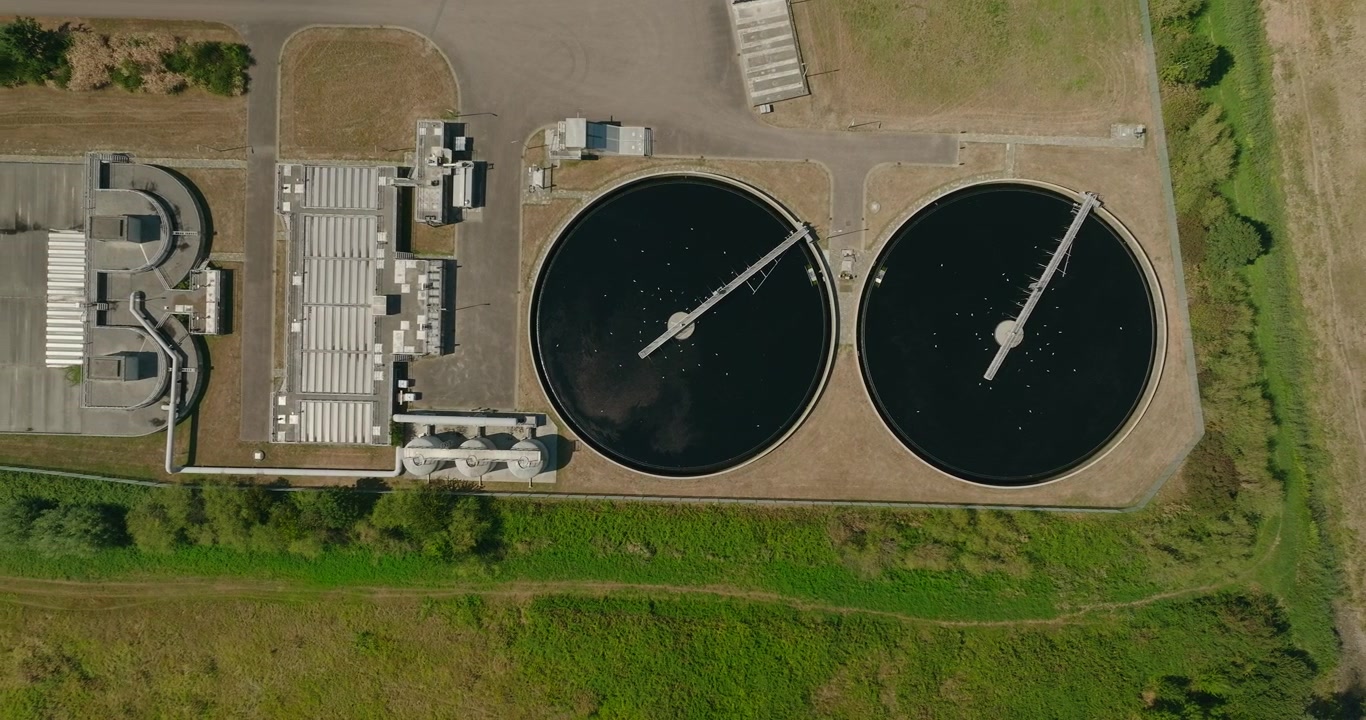 Top down aerial view of a wastewater treatment plant surrounded by the Dutch countryside, showing water purification infrastructure, two treatment basins and sustainable water management.