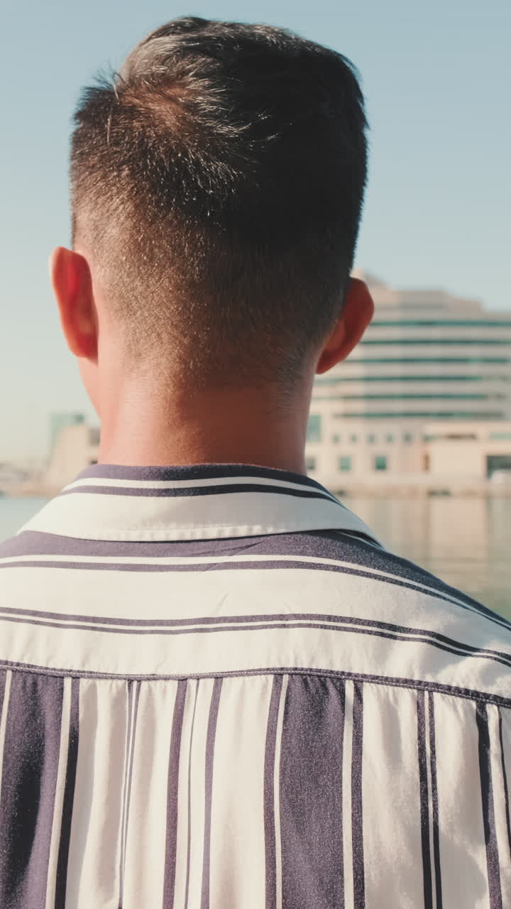 Man in striped shirt looking at building and water