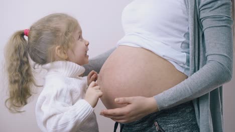 little girl has fun with young pregnant mommy in lit room