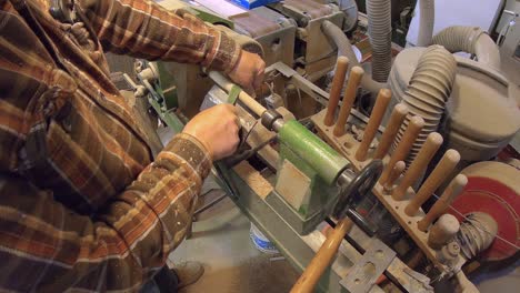 man's hands are sanding wooden dowel rod on turning wooden lathe