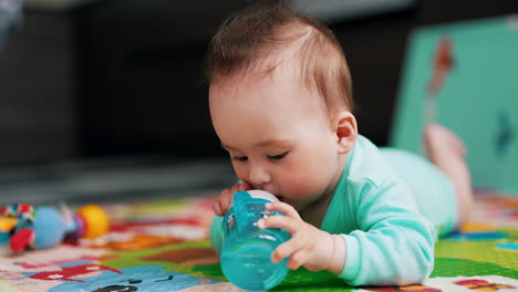 little baby boy is busy dealing with bottle. lovely kid with nice hairdo tries to drink water by himself. close up.