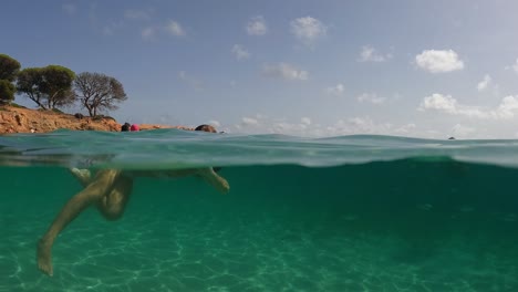 Waterline-scenic-view-of-little-girl-swimming-in-crystal-clear-tropical-seawater-of-Palombaggia-beach-in-Corsica-island,-France