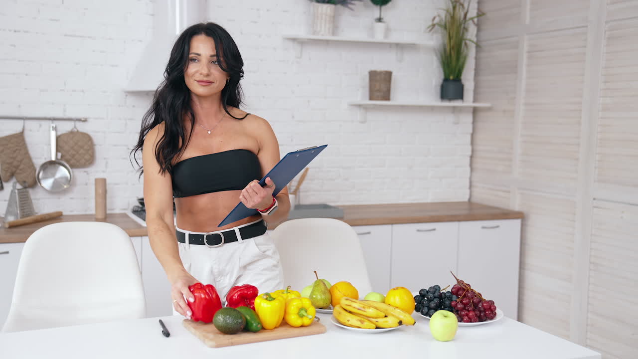 Healthy food at home. Happy brunette woman is making notes in modern kitchen. Vegan and vegetarian lifestyle. Food for slimming concept