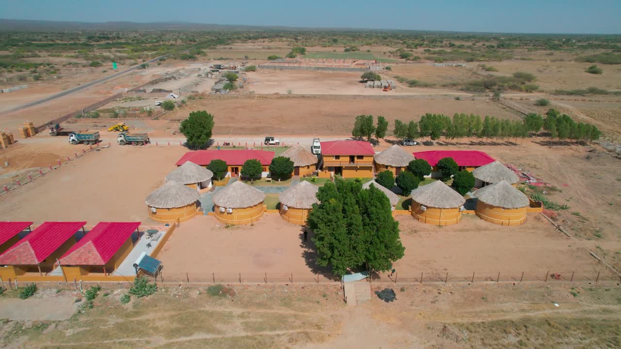 드론은 남아프리카의 황량한 사막 풍경에 둘러싸인 시골의 오두막과 목조 오두막을 촬영하여 거칠고 건조한 지형과 단순한 목조 구조물 사이의 극심한 대조를 강조합니다.