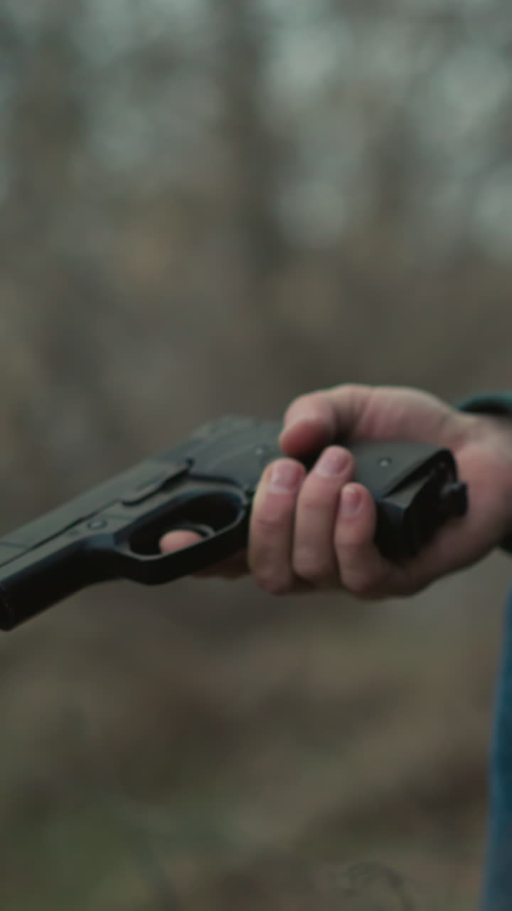 녹색 재과 파란 청바지를 입은 남자가 숲 속에 앉아 스마트폰에 깊이 집중하고 손에 총을 들고 아래로 향하고 있습니다.