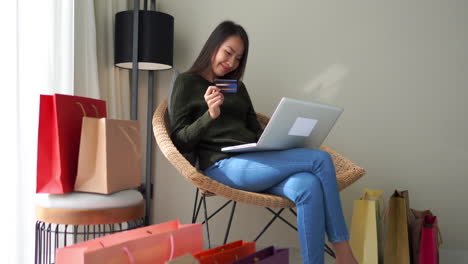 Joven-Mujer-Asiática-Comprando-En-Línea-Rodeada-De-Bolsas-De-Compras