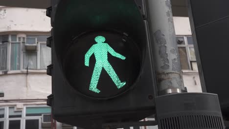 a pedestrian traffic light has the green light on for people to walk through a crossing zebra in hong kong.