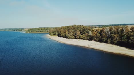a beautiful resting place with a wide river and a sandy beach near green and long fields. aerial view. camera motion to back.