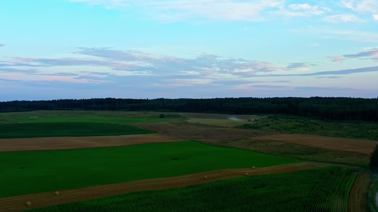 Rural gravel road winding through green and brown fields under evening sky