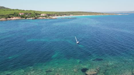 Solo-Segler-Segelt-Am-Strand-Von-Cala-Spinosa-In-Sardinien,-Italien-Entlang---4k-Antenne-Rückwärts