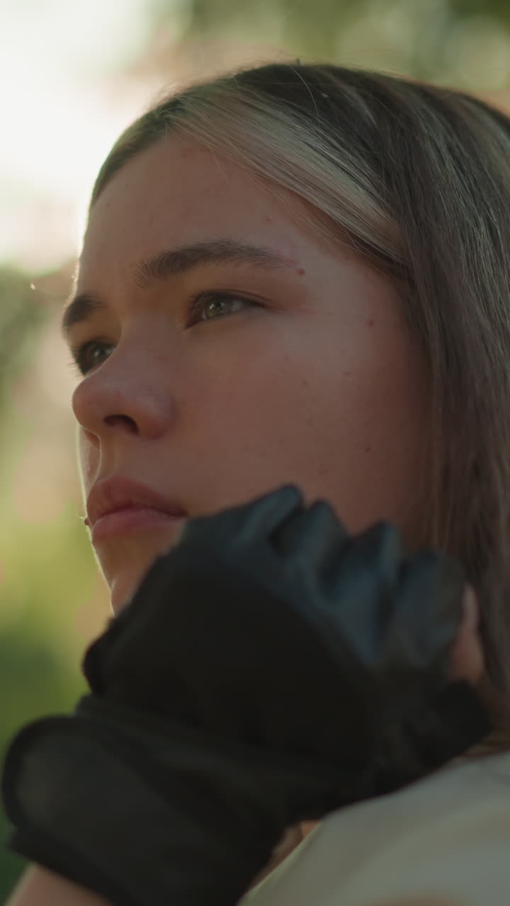 hermosa mujer joven descansando el mentón en la mano, mirando pensativamente en la distancia con la luz del sol creando un efecto de halo cálido alrededor de su cara, vegetación borrosa en el fondo