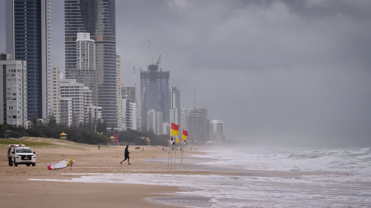 Life saver removing flags on the beach during heavy storms over beaches on the Gold Coast causing rough seas and rain, Gold Coast, Australia.