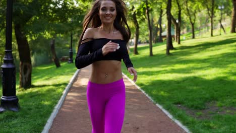 Happy-smiling-woman-in-sporty-bra-running-in-the-sunny-city-park-exercising-outdoors.-Steadicam-stabilized-shot,-Slow-Motion