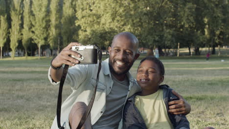 Padre-E-Hijo-Tomándose-Selfie-En-El-Parque,-Haciendo-Muecas.