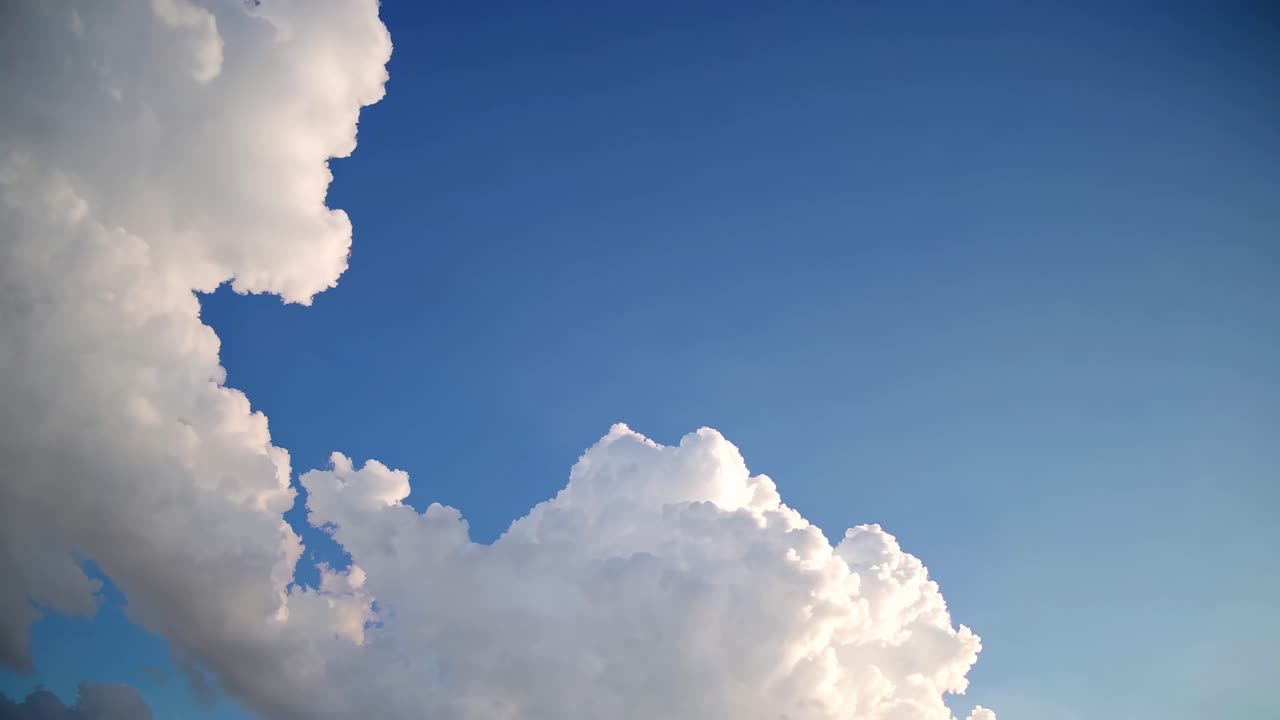 A serene video of fluffy white clouds against a clear blue sky, captured from a low angle