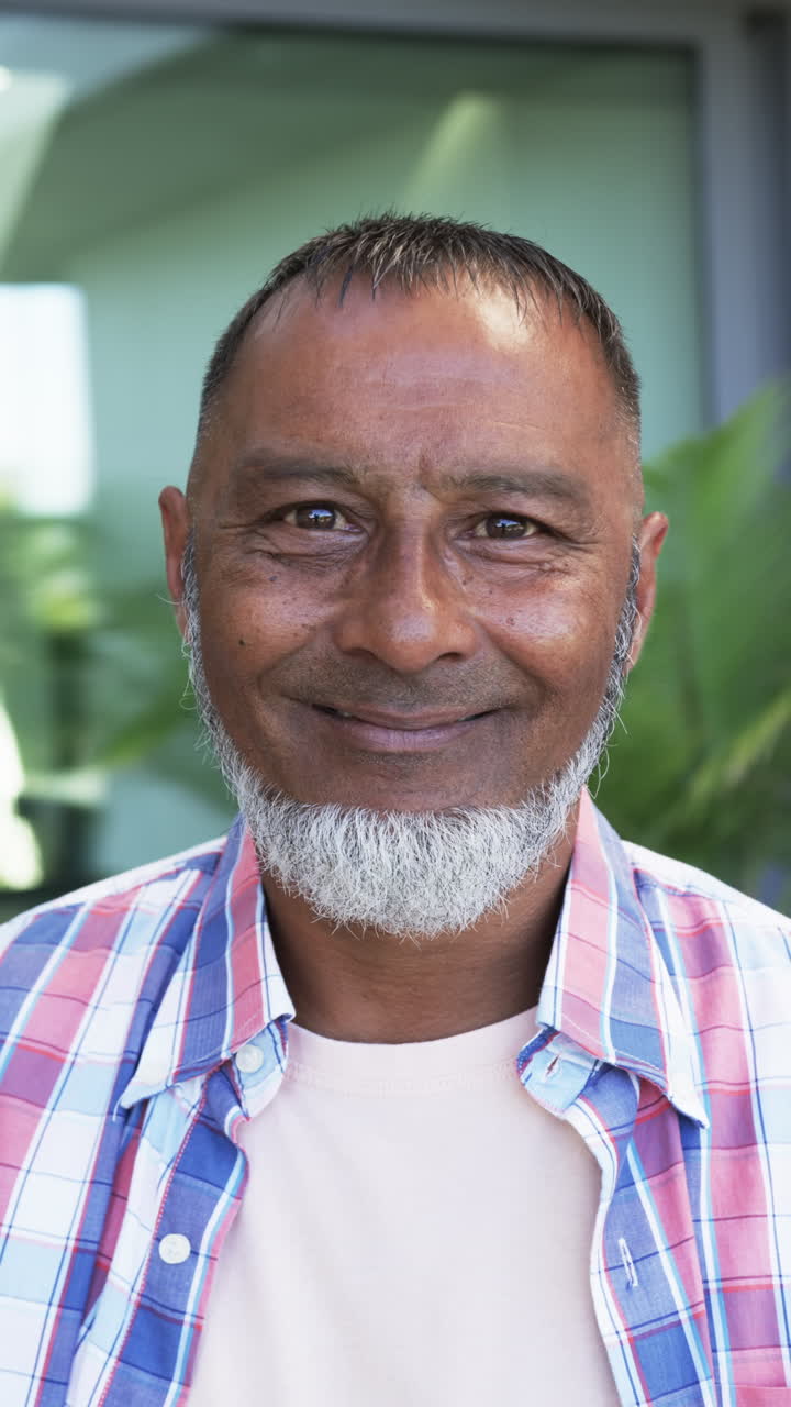 Vertical video: Smiling elderly man with white beard wearing plaid shirt, looking at camera