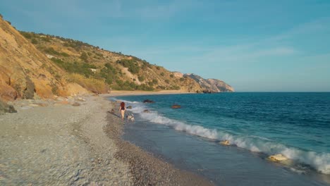 Drone-moving-backwards-at-the-beach-with-woman-walking-the-dogs-on-the-opposite-direction