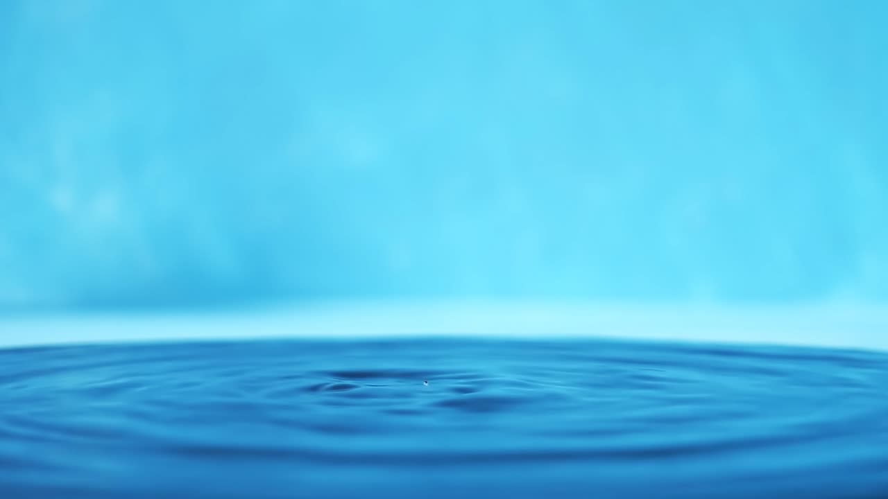 파란색 배경에 떨어지는 물방울과 함께 물 표면의 느린 모션 4k 비디오.