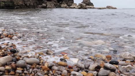 a slider shot of some waves crashing against a pebbly shore