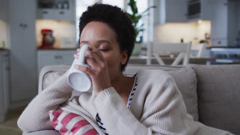 mixed race woman sitting on couch and drinking coffee