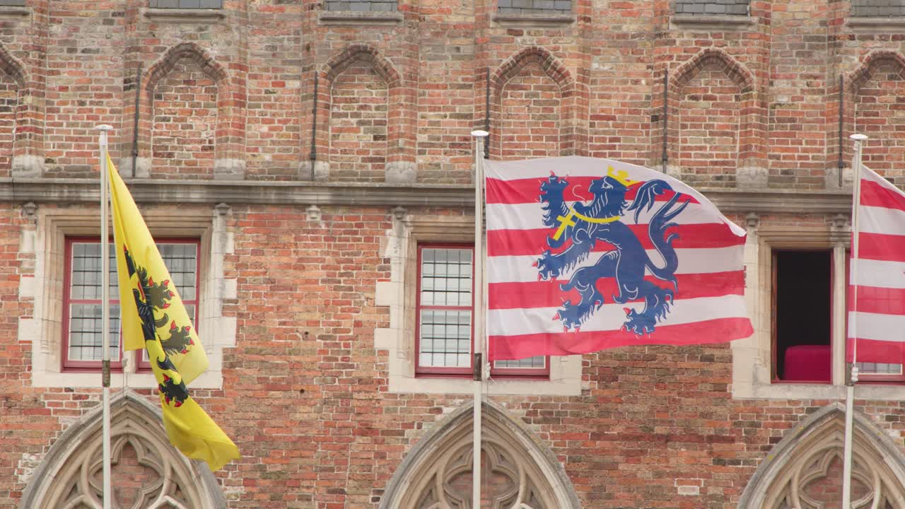 Colorful flags flutter against a medieval brick facade with gothic windows in overcast daylight