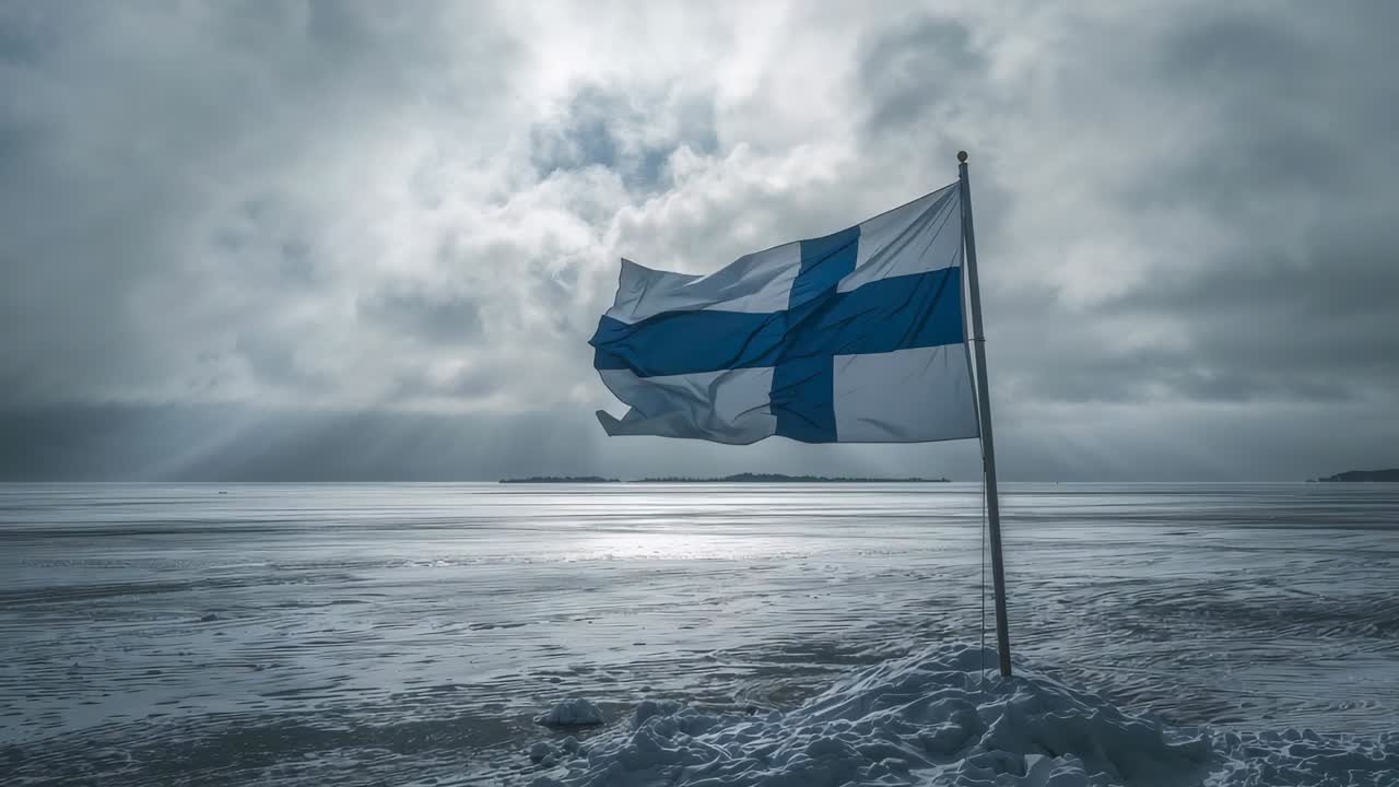 Fluttering Finnish flag on metal pole responding to steady gusts at snowy coastal shore, copy space