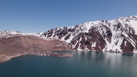 calm blue waters of el yeso dam surrounded by snowy mountains in chile