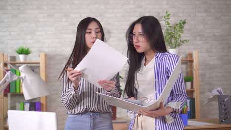 two young asian girls office workers discuss documents in the office