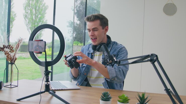 Vlogger uomo in diretta streaming recensisce una fotocamera a casa, video registrato con telefono cellulare.