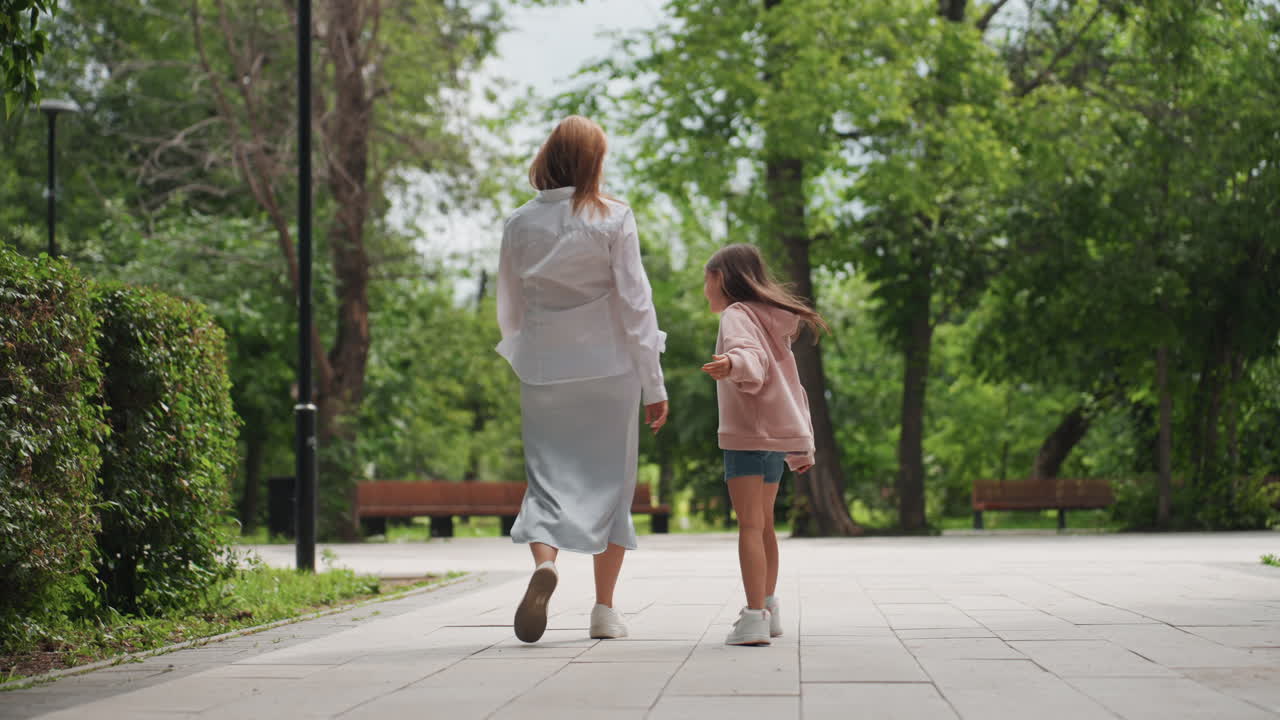 Samen wandelen door een weelderige omgeving. Zij aan zij slenteren over een vredig parkpad met groen. Moeder en dochter genieten van een serene wandeling langs een bladerrijk pad met een bankje in de buurt.