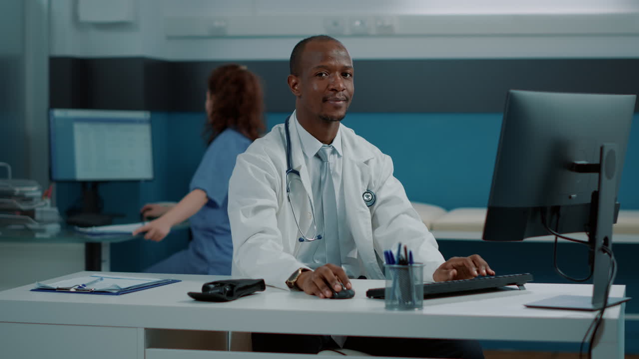 Medico che lavora alla scrivania nel suo studio con un infermiere sullo sfondo