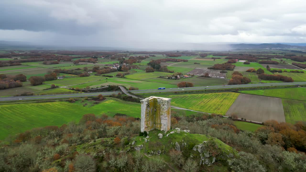 High angle aerial orbit of sandi&aacute;s tower, ourense, spain, above farmland on stormy day