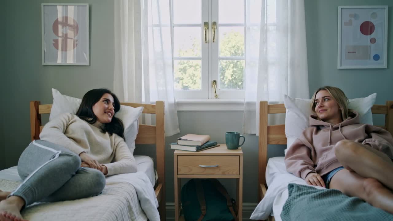 Making eye contact, chatting two women catching up in shared bedroom, showing books and mug