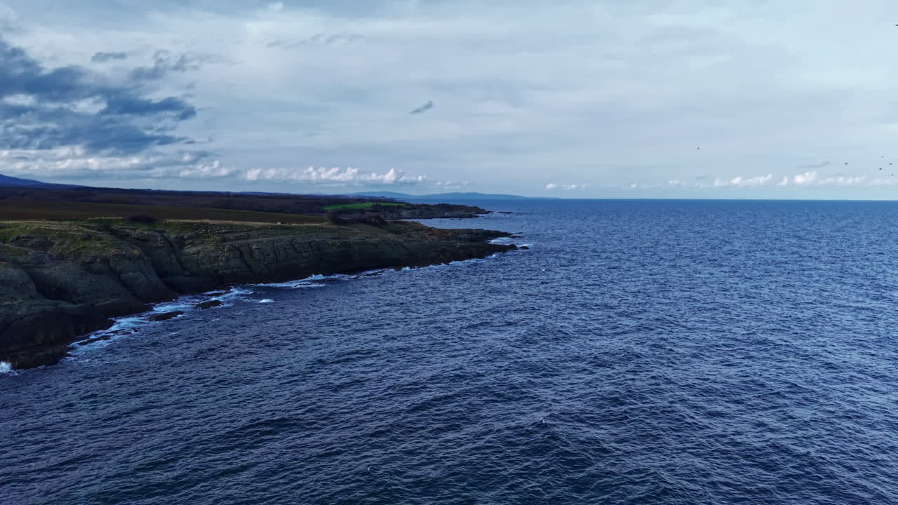 Unos acantilados costeros se encuentran con el océano azul infinito en un día sereno