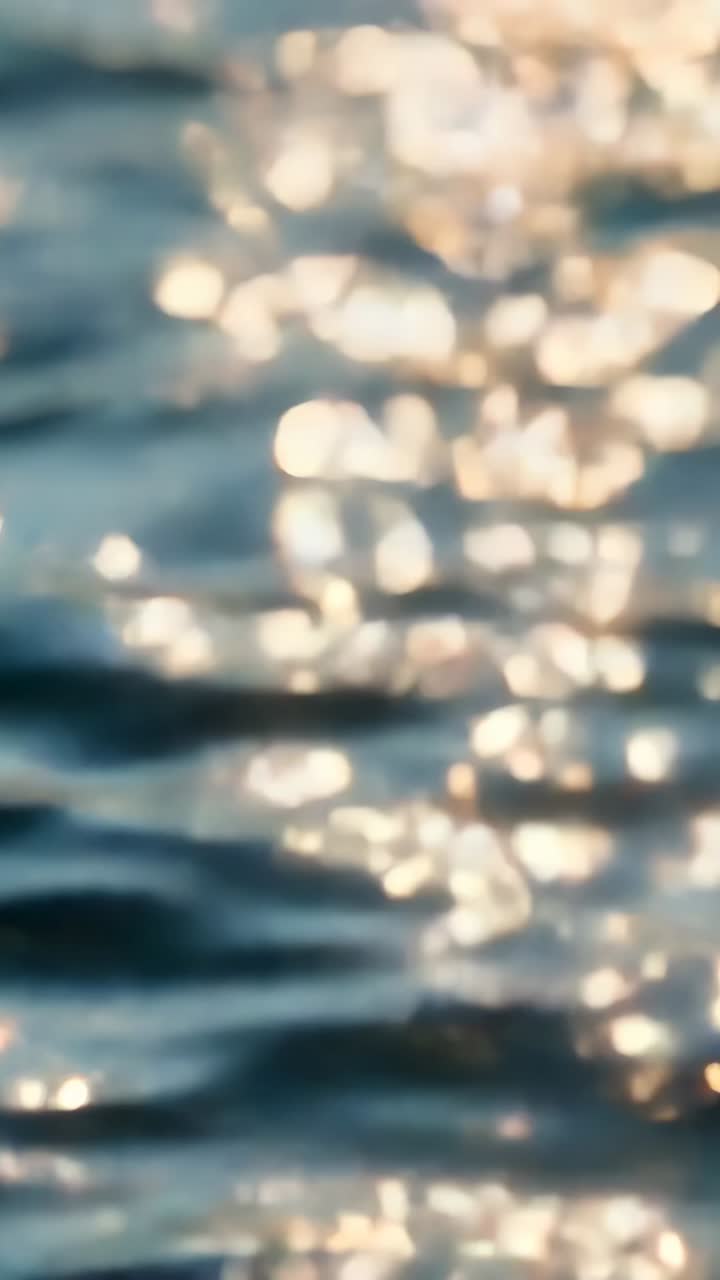 Vertical video: Shimmering water rippling in closeup, with wave rotation changing sunlight bokeh