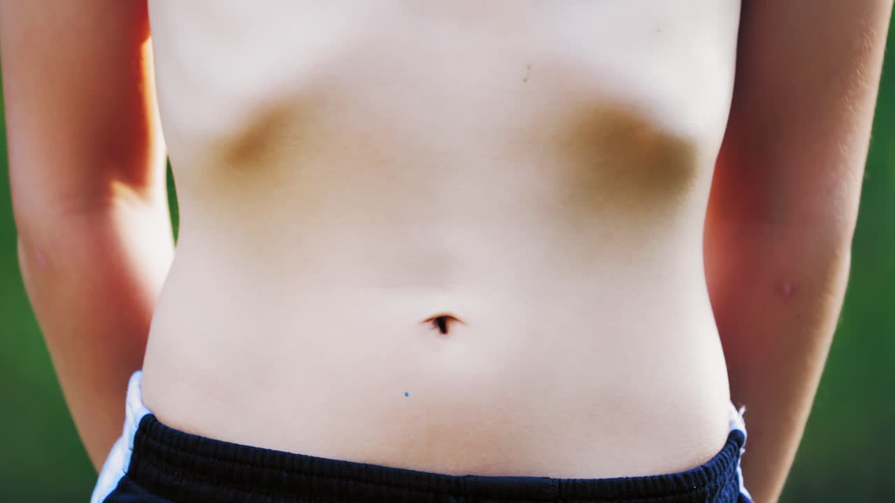 Boy's stomach breathing. Close-up of teenager's body in shorts isolated on green background. Healthy boy shows his belly.