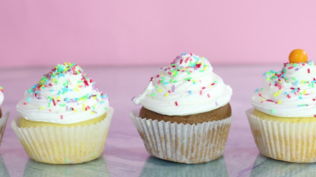 Putting colorful candies on delicious cup cakes with white cream for party