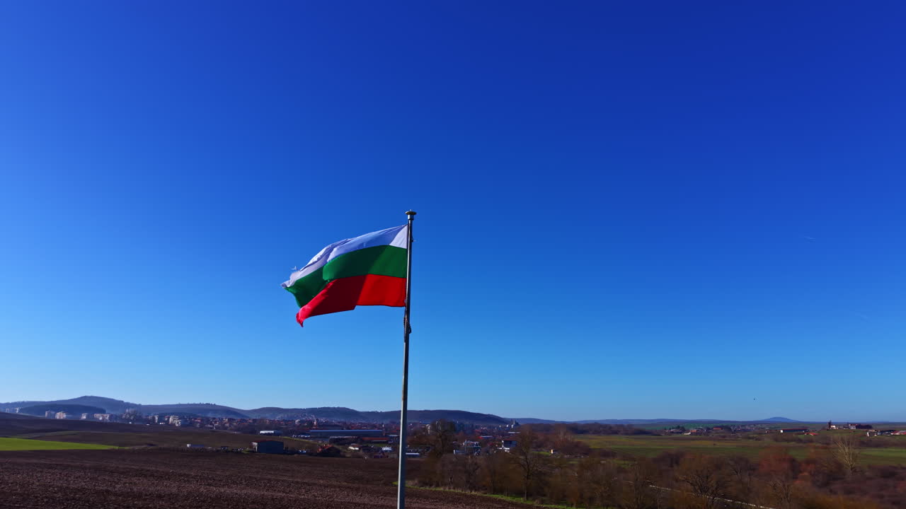 Bandiera bulgara che sventola al vento su un pennone in un paesaggio verde sotto un cielo azzurro limpido durante le ore diurne