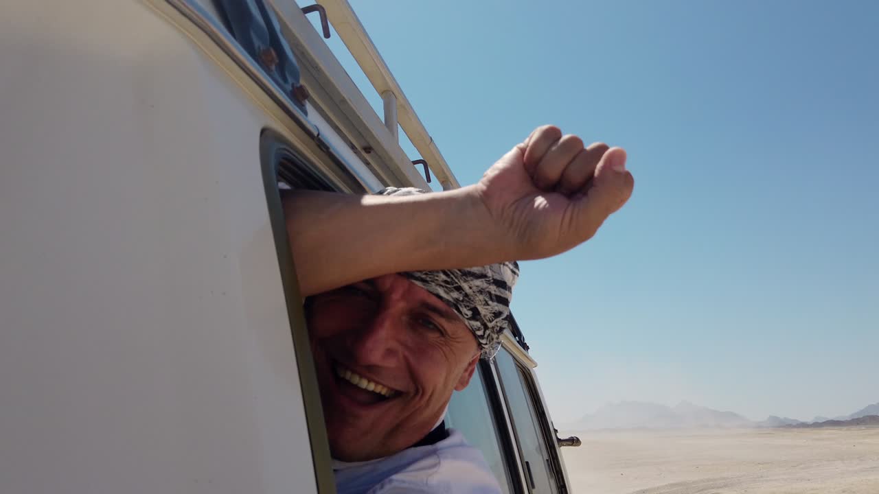 hombre árabe loco disfrutando de un rápido suv en un safari en el desierto. cabeza fuera de la ventana sonriendo y gritando excitado, cámara lenta