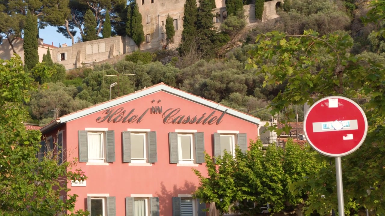 Statische Aufnahme eines rosa Hotelgebäudes unterhalb einer Steinburg bei hellem Sommerlicht