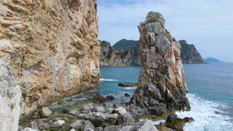 Aerial,-low,-close-fly-by-along-rocky-cliff-beach-on-Corfu,-Greece,-slow-motion