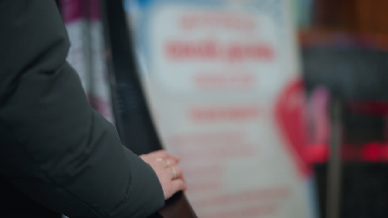 黒いフーディを着た手のクローズアップ動くエスカレーターのレールに寄りかかっている背景がぼやけている物体に書かれた不明確な文字忙しいショッピングモールの囲気を捉えている