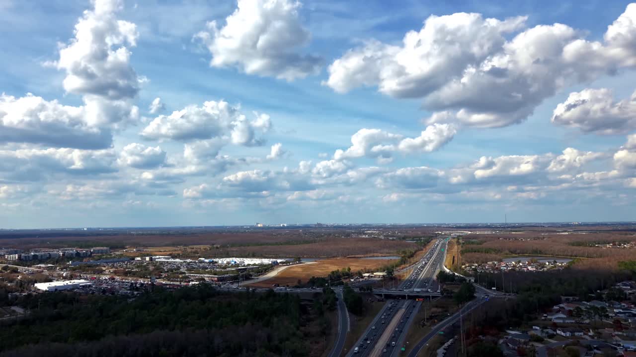 An aerial hyper lapse of Florida's Turnpike on a sunny day with clouds casting shadows. The camera dolly in and boom up along the highway showing the movement of the passing vehicles driving by